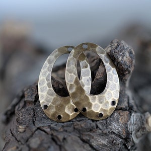 K&ouml;nnte beinhalten: Zwei ovale Metall-Anh&auml;nger mit geh&auml;mmerter Textur und Messing-Finish. Jeder Anh&auml;nger hat vier kleine L&ouml;cher am Rand.