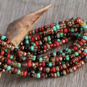 May include: A strand of colourful seed beads in shades of red, orange, brown, turquoise, and black. The beads are strung on a clear thread and are arranged in a random pattern.