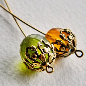 May include: Two gold-toned metal bead caps with intricate floral designs. One bead cap is green and the other is amber.
