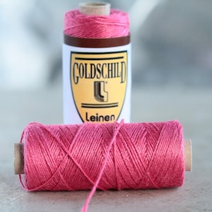 May include: A spool of pink linen thread with a label that reads "Goldschild Leinen".