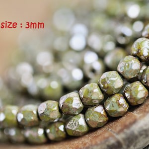 May include: Close-up of a strand of green glass beads with a metallic sheen. The beads are faceted and have an irregular shape. The beads are approximately 3mm in size.  size: 3mm