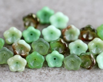 May include: A collection of green glass flower-shaped beads with a slight iridescent sheen. The beads have a small hole in the center for stringing.