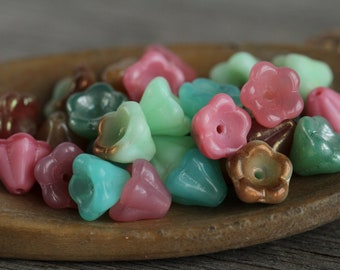 May include: A collection of colorful glass beads in pink, green, and brown shades. The beads are shaped like flowers and have a glossy finish.