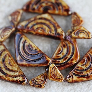 May include: A strand of brown and cream triangular ceramic beads with a swirling pattern. The beads are strung on a brown cord.