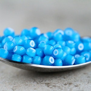 Puede incluir: Una cuchara llena de peque&ntilde;as cuentas de vidrio azul claro con un anillo blanco alrededor del centro de cada cuenta.