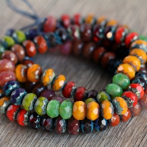 Op de afbeelding: Een streng gekleurde facetgeslepen edelsteen kralen in tinten van rood, oranje, geel, groen, blauw en paars. De kralen zijn geregen aan een koord en zijn gerangschikt in een cirkelvormig patroon.
