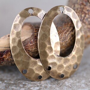K&ouml;nnte beinhalten: Zwei ovale Metall-Anh&auml;nger mit geh&auml;mmerter Textur und Messing-Finish. Jeder Anh&auml;nger hat drei L&ouml;cher zum Anbringen an Schmuck oder andere Bastelarbeiten.