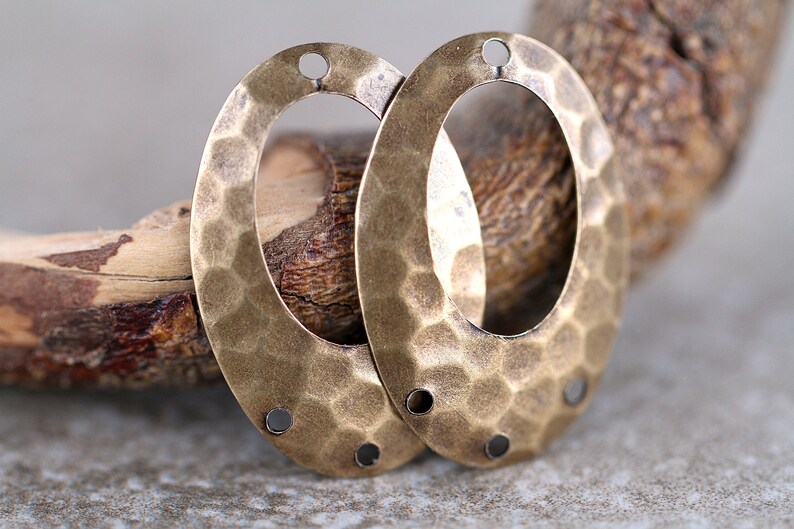 K&ouml;nnte beinhalten: Zwei ovale Metall-Anh&auml;nger mit geh&auml;mmerter Textur und Messing-Finish. Jeder Anh&auml;nger hat drei L&ouml;cher zum Anbringen an Schmuck oder andere Bastelarbeiten.