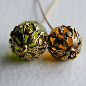 May include: Two gold-toned metal bead caps with intricate floral designs. One bead cap is green and the other is amber.