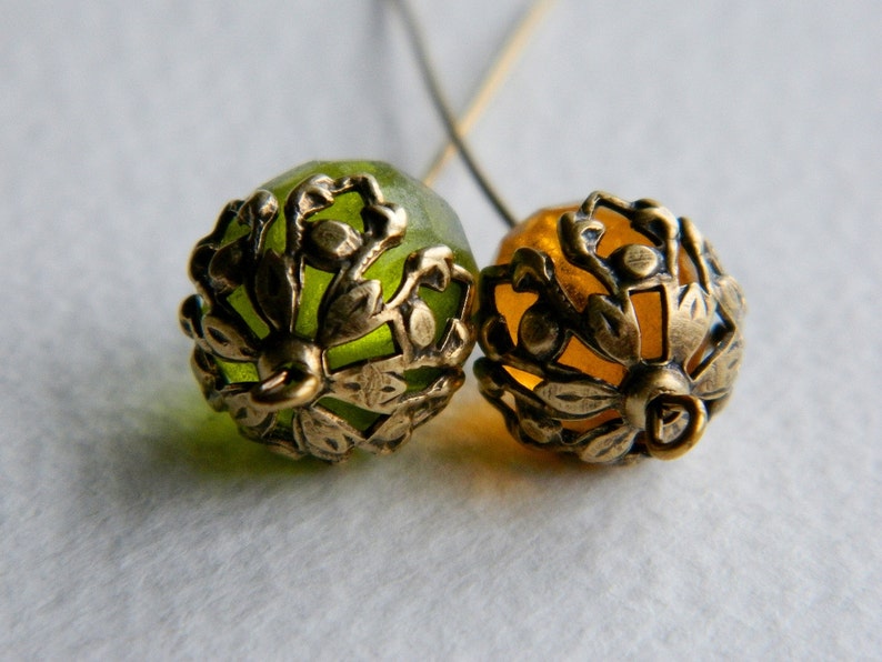 May include: Two gold-toned metal bead caps with intricate floral designs. One bead cap is green and the other is amber.