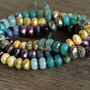 May include: A multi-coloured strand of glass beads with a mix of blue, green, purple, and yellow tones. The beads are faceted and have a glossy finish.
