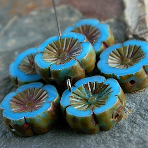 May include: A cluster of six flower-shaped beads. Each bead features a vibrant turquoise blue petal edge, a brown center with radial grooves, and a weathered, earthy green-brown exterior. The beads are strung together with a silver wire.
