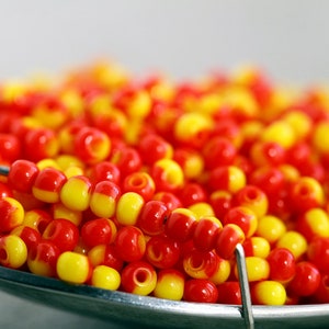 May include: A close-up of a bowl filled with red and yellow beads. The beads are small and round, and they are arranged in a random pattern.