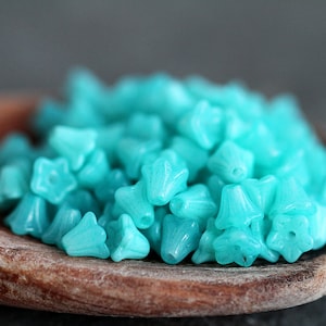 May include: A wooden spoon filled with turquoise blue glass beads in the shape of a flower.