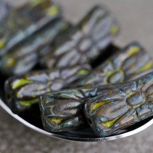 Peut inclure: Gros plan sur plusieurs perles en verre bleu, vert et jaune avec un motif floral. Les perles sont disposées dans une cuillère.