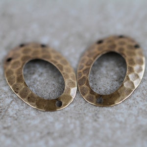 K&ouml;nnte beinhalten: Zwei ovale Metall-Anh&auml;nger mit geh&auml;mmerter Textur. Die Anh&auml;nger sind hellgoldfarben und haben oben ein Loch zum Anbringen an Schmuck.