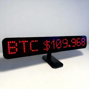 May include: A black LED display showing "BTC $109.968" in red lights. The display is mounted on a small black stand. The background is plain white. Ideal for displaying cryptocurrency information.
