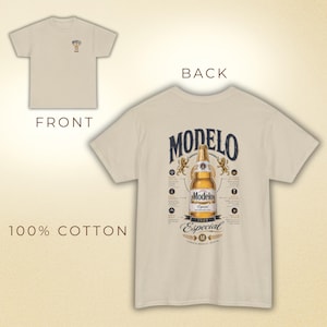 May include: Beige, short-sleeved t-shirt. The front features a small Modelo logo, while the back displays a large Modelo Especial beer bottle graphic with text and design elements. The shirt is made of 100% cotton.