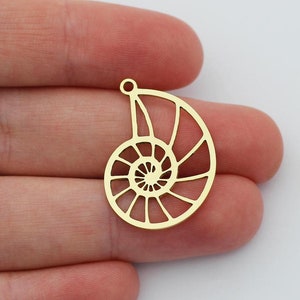 Könnte beinhalten: Zwei goldfarbene Metall-Anhänger in Form von Nautilus-Schalen. Die Anhänger sind ausgeschnitten und haben ein filigranes, kompliziertes Design.
