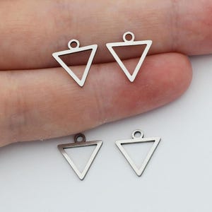 Puede incluir: Cuatro abalorios de plata en forma de triángulo con un bucle en la parte superior. Los abalorios están dispuestos en dos pares, con los abalorios más grandes en la parte superior y los más pequeños en la parte inferior.