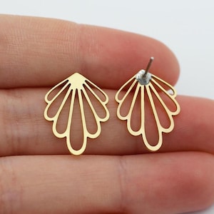 May include: A pair of gold-colored stud earrings. Each earring features a fan-shaped design with multiple curved lines radiating from a central point. The earrings are displayed on a light background.