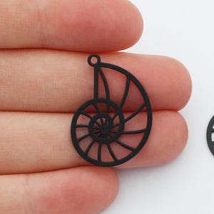 May include: Two black metal nautilus shell charms with a cutout design. The charms have a hole at the top for attaching to jewelry or other crafts.