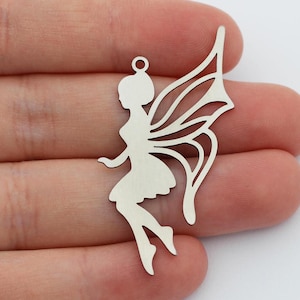 May include: Silver metal charm featuring a cutout silhouette of a fairy with wings. The fairy is sitting with her legs crossed and her wings are spread out behind her.