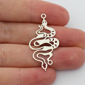 Peut inclure: Breloque en métal argenté avec un motif découpé détaillé d'un serpent enroulé sur lui-même. Le breloque a une boucle en haut pour l'attacher à des bijoux ou d'autres objets artisanaux.