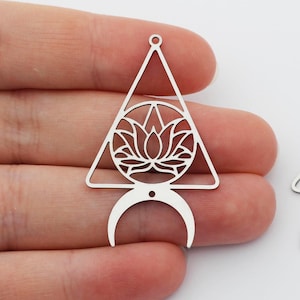 Puede incluir: Dos amuletos de metal plateado en forma de triángulo con una luna creciente en la parte inferior. El triángulo presenta un diseño recortado de una flor de loto.