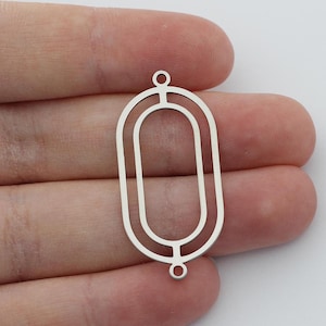 May include: Two silver oval-shaped metal frames with a smaller oval cutout inside. The frames have a small loop at the top for hanging.