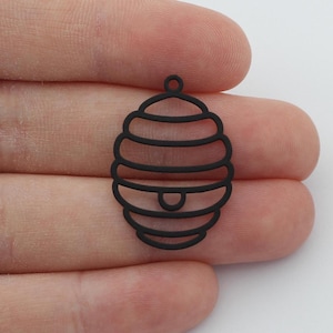 May include: Black metal charm shaped like a beehive. The charm is detailed with a series of concentric circles and a small opening at the top.