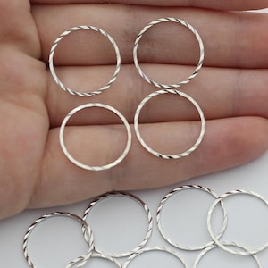 Puede incluir: Se muestra una colección de anillos de metal plateado, algunos con un diseño de cuerda trenzada. Los anillos son circulares y varían en textura. La imagen está tomada desde una perspectiva cercana, destacando los detalles de la joyería.