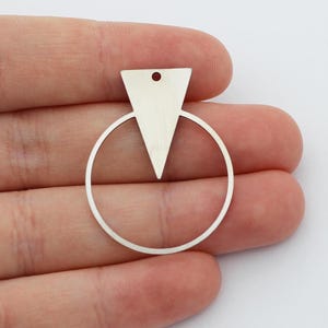 Puede incluir: Pendiente de plata con un círculo y un colgante triangular.
