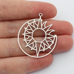 May include: Silver charm featuring a sun and moon design. The sun is a circular design with a starburst pattern and the moon is a crescent shape.