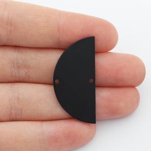 May include: Two black metal half-circle shapes with two holes each. The half-circles are flat and have a smooth, matte finish.