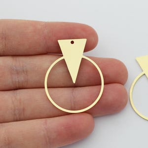 May include: Two gold-toned metal earring blanks with a circle and a triangle shape. The triangle is centred inside the circle and has a small hole at the top.
