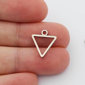 May include: Two silver-colored, open-frame triangle charms with a small loop at the top for attaching to jewelry. One charm is held by a person's fingers. The charms are on a white background.