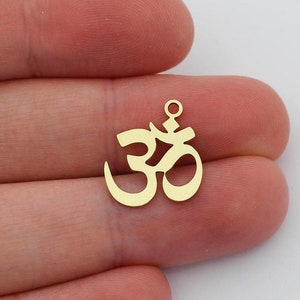 Puede incluir: Dos abalorios de metal de color dorado en forma de símbolo Om. Los abalorios miden aproximadamente 2,5 cm y tienen un agujero en la parte superior para sujetarlos a un collar o pulsera.