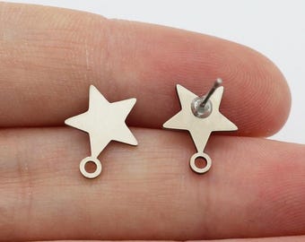 May include: Two silver star-shaped earring findings with a loop at the bottom. The findings are shown on a hand.