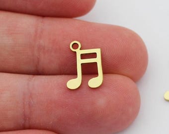 Pode incluir: Dois pingentes de metal dourado em forma de nota musical. Os pingentes têm a forma de uma clave de sol e medem aproximadamente 2,5 cm de comprimento.