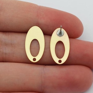 May include: A pair of gold oval-shaped earring blanks with a hole in the center. The earring blanks are held in a hand.