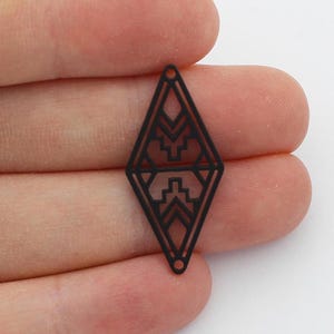 Puede incluir: Dos dijes de metal negro en forma de diamante con un patrón geométrico. Los dijes están recortados y tienen un diseño delicado.