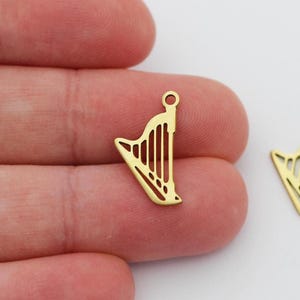May include: Two gold-colored metal harp charms. The charms are in the shape of a harp and have a hole at the top for attaching to a chain or bracelet.