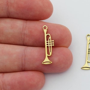 Puede incluir: Dos abalorios de trompeta de color dorado, cada uno con un contorno detallado de una trompeta, perfectos para añadir un toque musical a los proyectos de joyería.