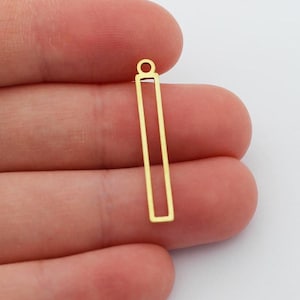 May include: Two gold-colored rectangular charms with a small loop at the top for jewelry making. One charm is held in a hand, while the other is separate. The charms have a simple, open design.