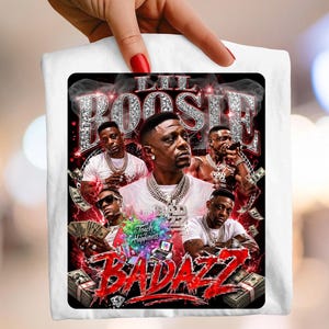 Puede incluir: Camiseta blanca con un diseño gráfico con el texto "Lil Boosie BADAZZ" en rojo y plata. El diseño incluye imágenes de Lil Boosie y montones de dinero. También se incluyen las palabras "Touch Happiness".