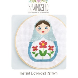 May include: Cross stitch pattern featuring a blue and white Russian nesting doll with red flowers. The pattern is framed in a wooden hoop and the text "SewingSeed Cross Stitch Goodness" and "Instant Download Pattern" is visible below the hoop.