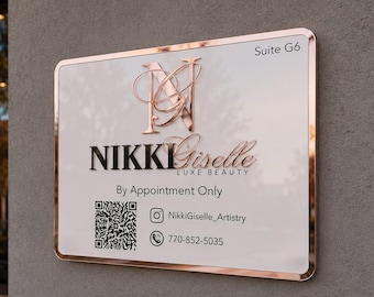 May include: A rectangular white sign with a rose gold metallic border and trim. The sign features the text NIKKI Giselle LUXE BEAUTY, Suite G6, By Appointment Only, a QR code, an Instagram icon with NikkiGiselle_Artistry, and a phone icon with 770-852-5035.