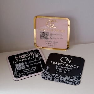 May include: Three square business cards. The top card is pink with gold trim and text that reads "GIBSON & GALINE". The second card is black with white floral accents and the text "bloom FLOWERS STUDIO". The third card is black with white floral accents and the text "BEAUTY SPACE".