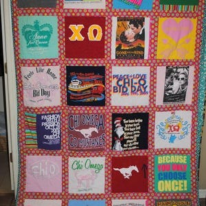 May include: A memory quilt constructed from twenty-four square fabric panels featuring various Chi Omega sorority graphics, text, and illustrations. The panels are separated by a bright pink fabric border with a repeating green and yellow dot pattern.